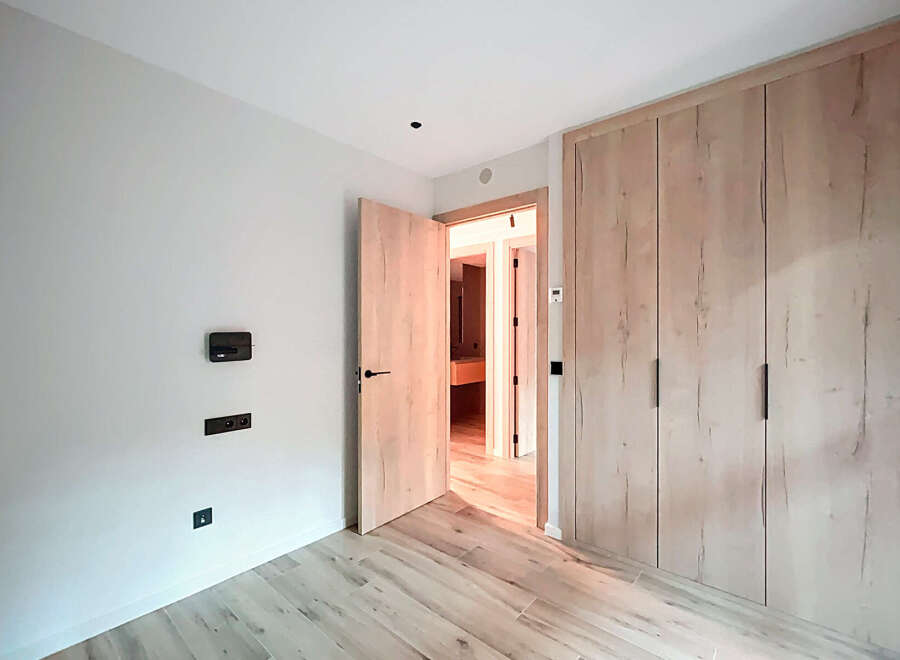 This modern bedroom boasts a sleek design with light wood flooring and matching built-in wardrobes, offering ample storage space.