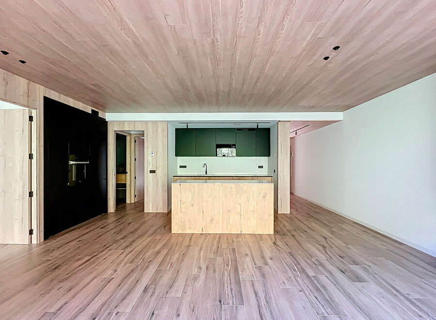 Stunning open-plan living space with light wood flooring and a modern kitchen featuring dark green cabinetry and a light wood island.