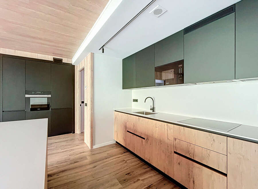 Modern kitchen with sleek dark green upper cabinets and light wood lower cabinets.
