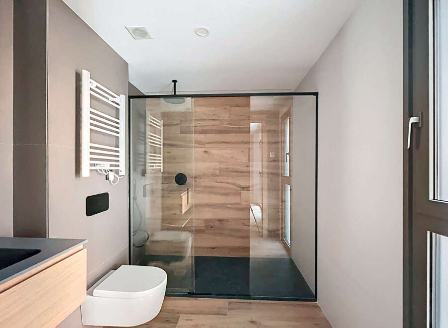 Modern bathroom with a sleek glass shower enclosure and wooden wall tiles.
