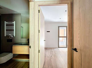 Modern bathroom with wooden vanity and heated towel rack, seamlessly connected to a bright and airy bedroom with large windows and light wood flooring.