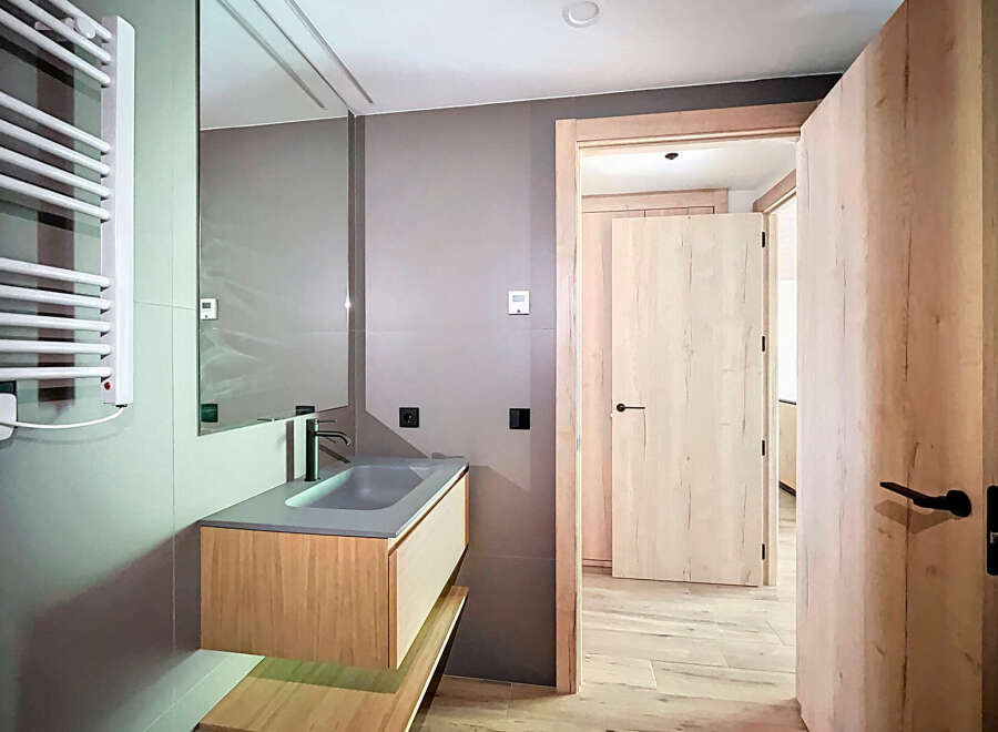 Modern bathroom with sleek gray sink and wooden vanity, complemented by a heated towel rack and stylish light wood doors.