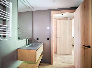 Modern bathroom with sleek gray sink and wooden vanity, complemented by a heated towel rack and stylish light wood doors.