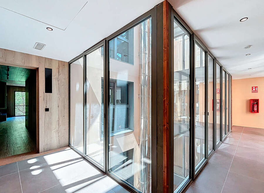 Modern hallway with floor-to-ceiling glass walls offering abundant natural light and views of the inner courtyard.