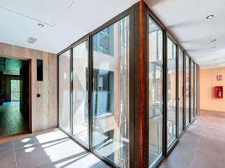 Modern hallway with floor-to-ceiling glass walls offering abundant natural light and views of the inner courtyard.