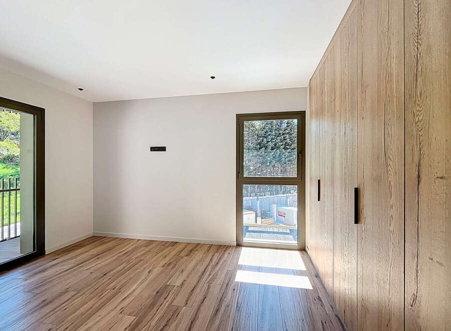 This modern bedroom boasts a sleek design with natural wood flooring and a large built-in wardrobe, offering ample storage space.