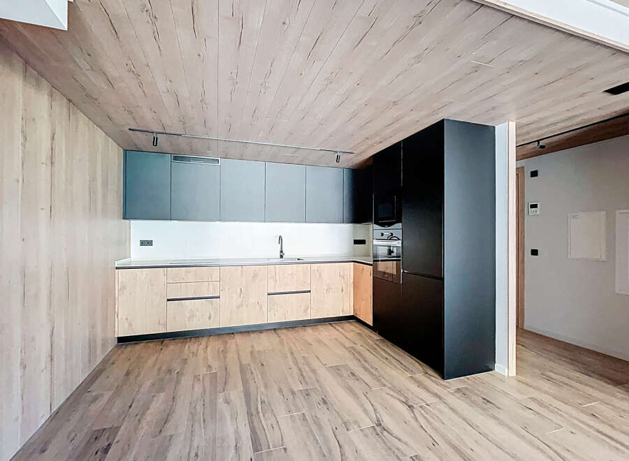 Modern kitchen with wooden ceiling and flooring, sleek dark cabinets, and light wood countertops.