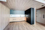 Modern kitchen with wooden ceiling and flooring, sleek dark cabinets, and light wood countertops.
