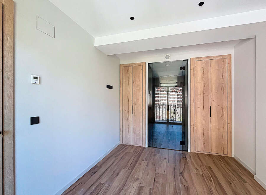 Modern apartment hallway with sleek glass and wood doors, offering ample storage space.
