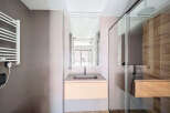 Modern bathroom with sleek gray tile, wooden vanity, and frameless glass shower enclosure.