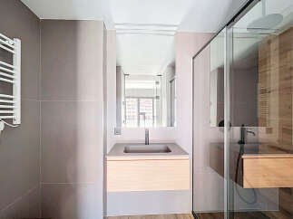 Modern bathroom with sleek gray tile, wooden vanity, and frameless glass shower enclosure.