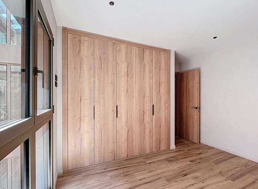This stunning bedroom boasts a spacious built-in wardrobe with sleek, light wood doors, offering ample storage.