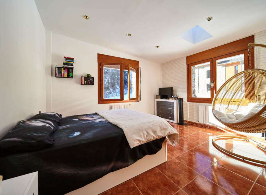 Cozy bedroom with a comfy bed, large windows offering mountain views, and a stylish hanging chair.