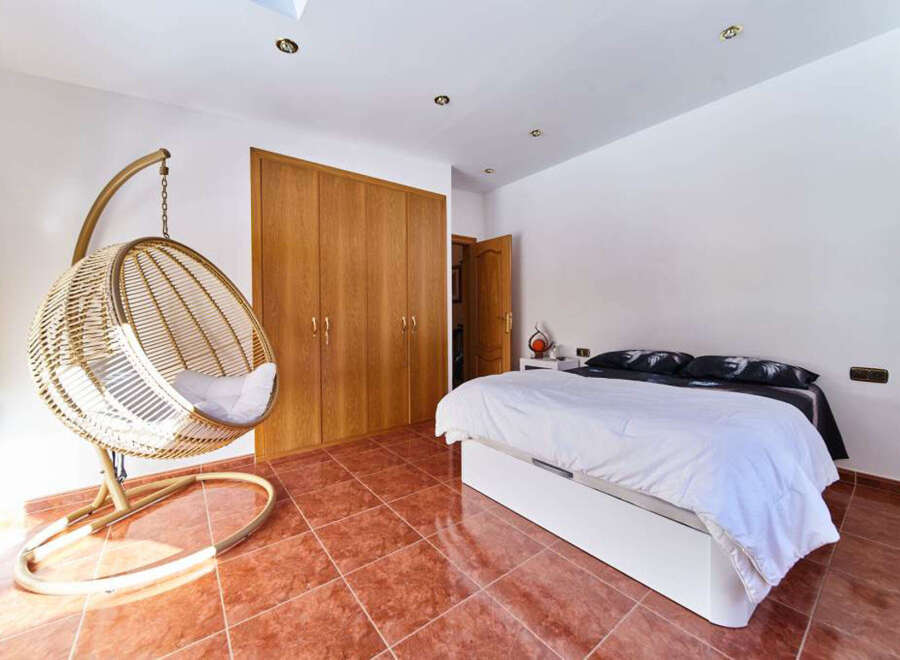 Relax in this stunning bedroom featuring a unique hanging chair and built-in wooden wardrobe.