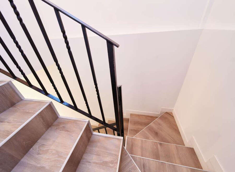 Modern staircase with sleek black metal railing and light wood flooring.