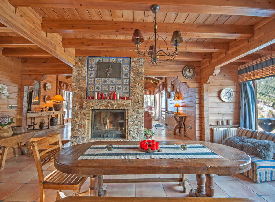 Rustic mountain chalet with a stunning stone fireplace, wooden beams, and large windows offering breathtaking views.