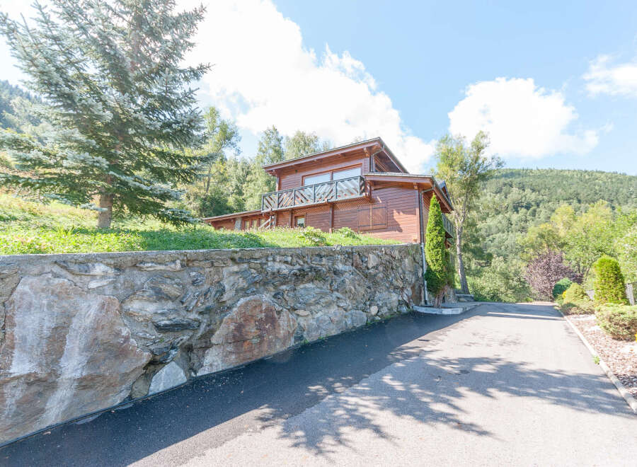 Mountain chalet with stone wall and paved driveway.