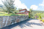 Mountain chalet with stone wall and paved driveway.