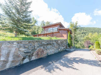 Mountain chalet with stone wall and paved driveway.
