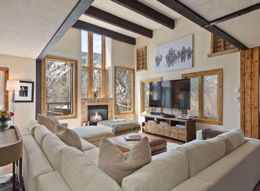 This stunning living room boasts a spacious sectional sofa, perfect for relaxing by the fireplace and enjoying the breathtaking mountain views through expansive windows.