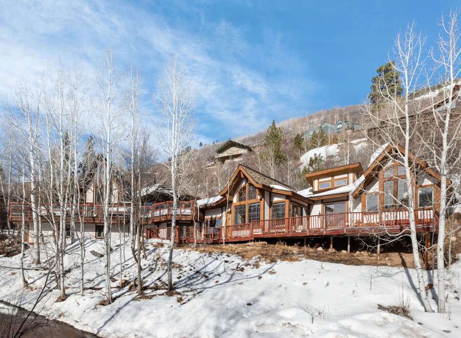Luxury mountain home nestled on a snowy hillside, boasting expansive decks with wooden railings offering breathtaking views.