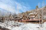 Luxury mountain home nestled on a snowy hillside, boasting expansive decks with wooden railings offering breathtaking views.