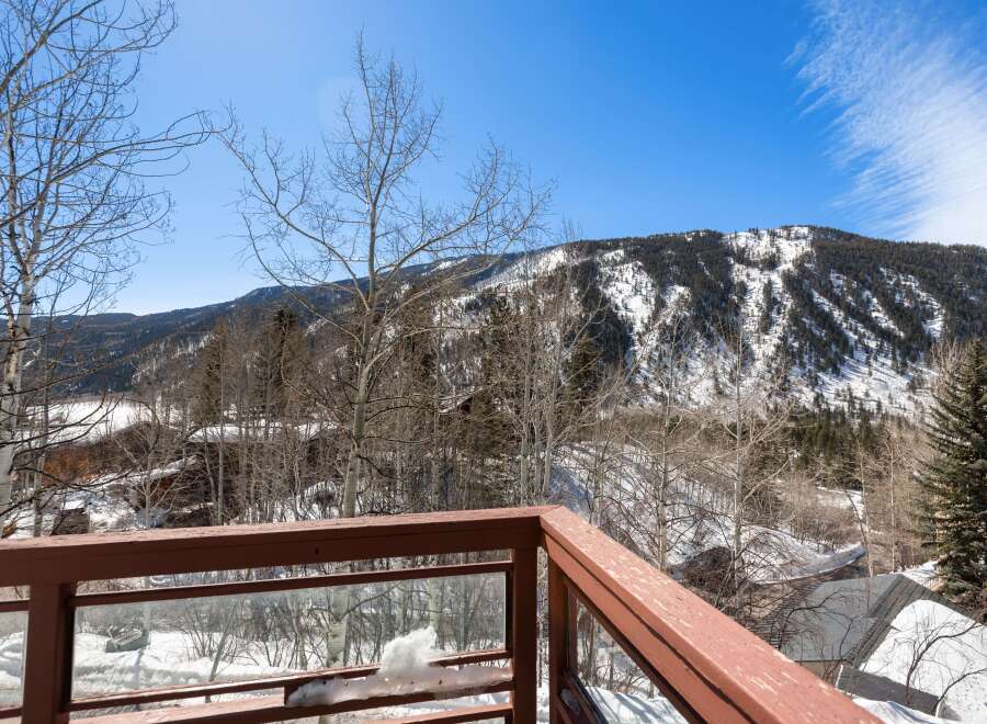 Mountain view from a deck with a wooden railing and glass panels.