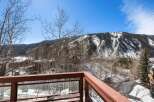Mountain view from a deck with a wooden railing and glass panels.