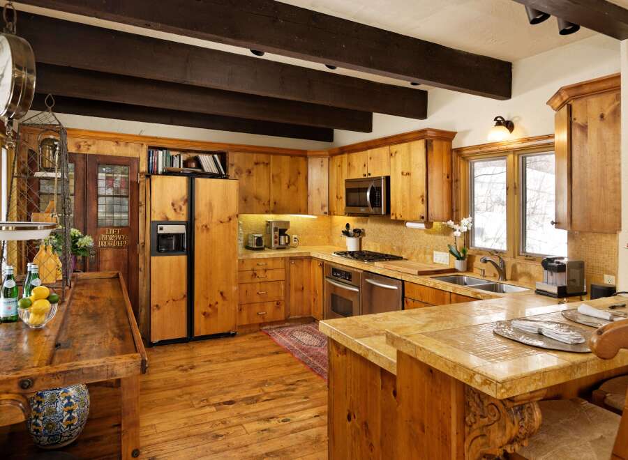 This charming kitchen boasts rustic wooden cabinetry, exposed beams, and a large island with seating, creating a warm and inviting atmosphere.