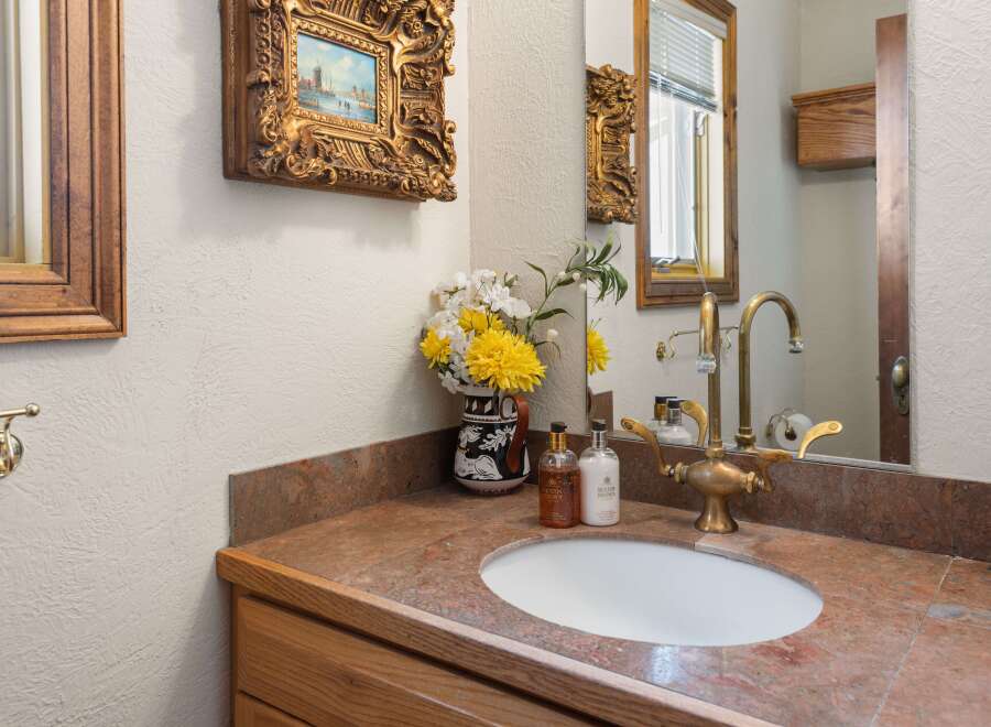 This charming bathroom boasts a vintage-style brass faucet and an oval sink, complemented by a granite countertop and wooden cabinetry.