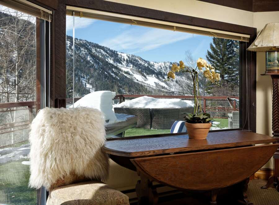 Mountain view home boasts a stunning vista through expansive windows, showcasing snow-capped peaks and a lush green lawn.
