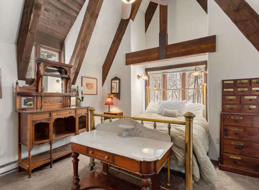 This charming bedroom boasts a unique blend of rustic and antique features, highlighted by exposed wooden beams and a brass bed frame.