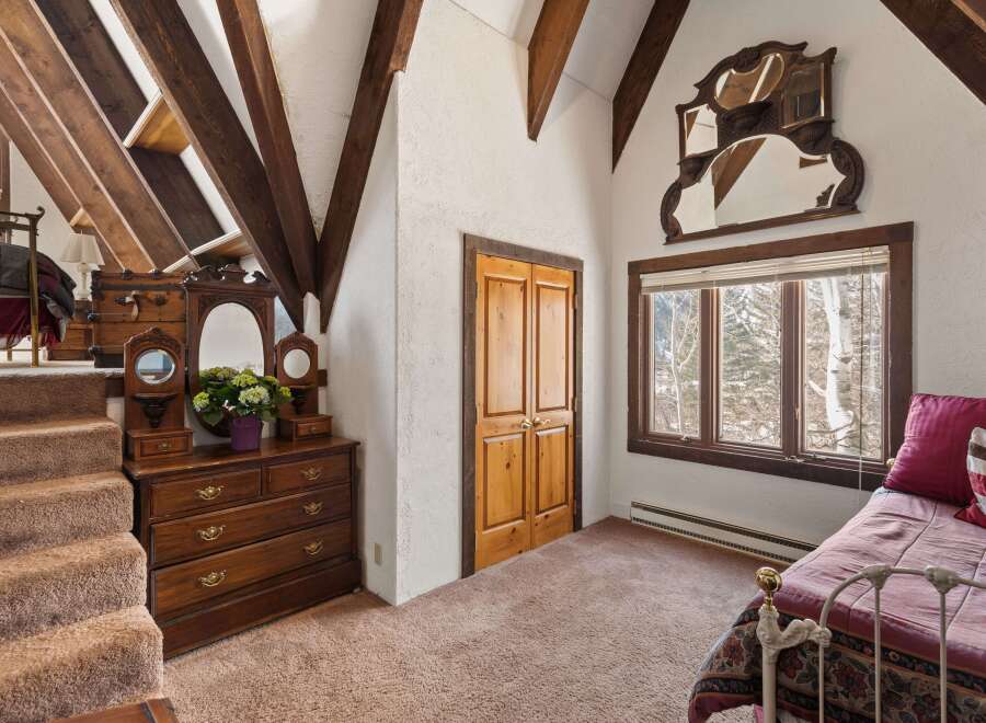 This charming bedroom boasts a cozy atmosphere with its unique sloped ceilings and exposed wooden beams.
