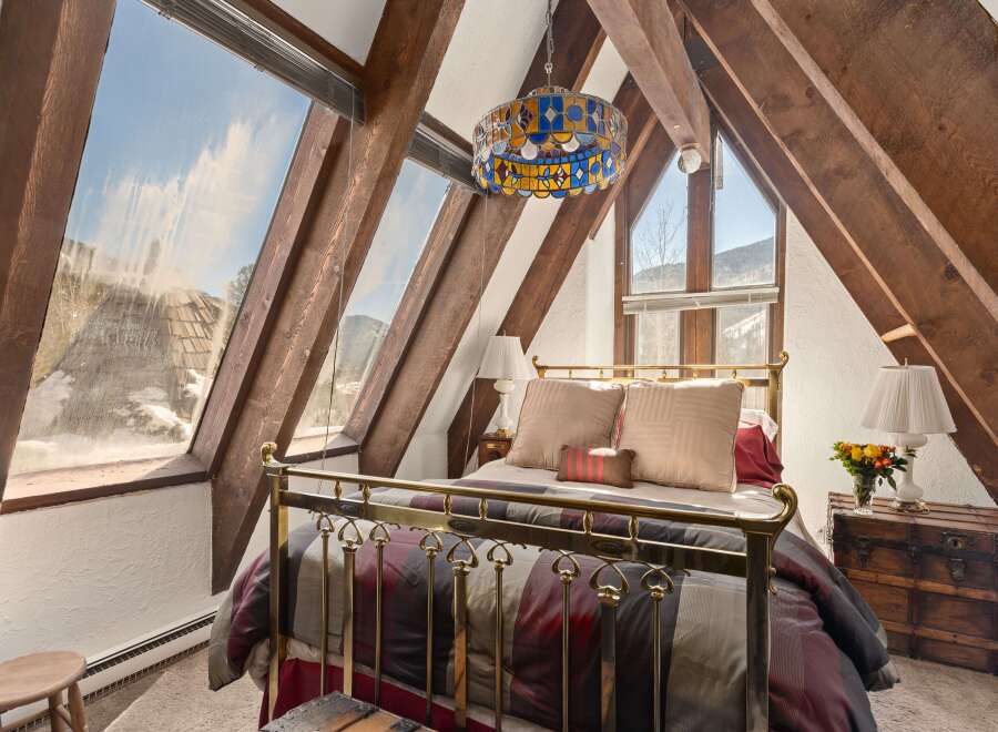 A cozy bedroom with a brass bed frame and stained-glass chandelier is nestled under a wood-beamed ceiling.