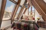 A cozy bedroom with a brass bed frame and stained-glass chandelier is nestled under a wood-beamed ceiling.