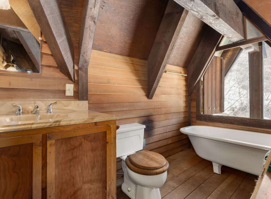 Rustic bathroom with wood walls and beams, featuring a clawfoot tub, wooden vanity, and toilet.