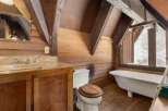Rustic bathroom with wood walls and beams, featuring a clawfoot tub, wooden vanity, and toilet.