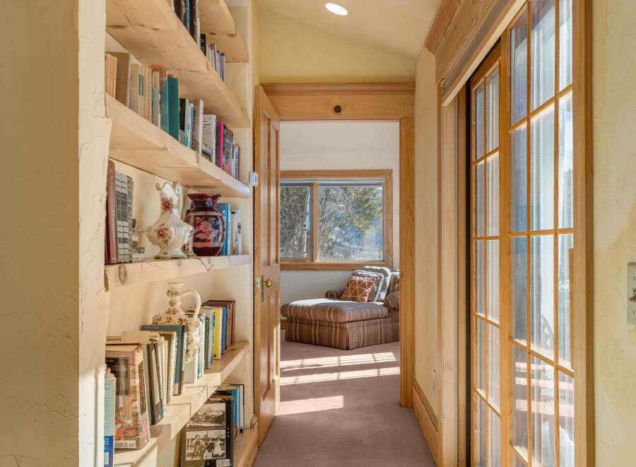 Sunlit hallway with built-in bookshelves and sliding glass doors leading to a relaxing lounge area.