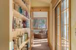 Sunlit hallway with built-in bookshelves and sliding glass doors leading to a relaxing lounge area.