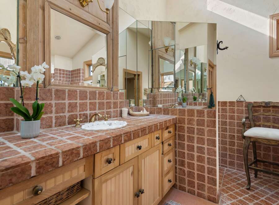 This luxurious bathroom boasts a stunning brick tile design, complemented by elegant wooden cabinetry and ornate mirrors.