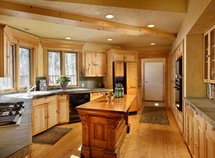This stunning kitchen boasts a rustic-chic design with knotty pine cabinets, exposed wood beams, and a large island.