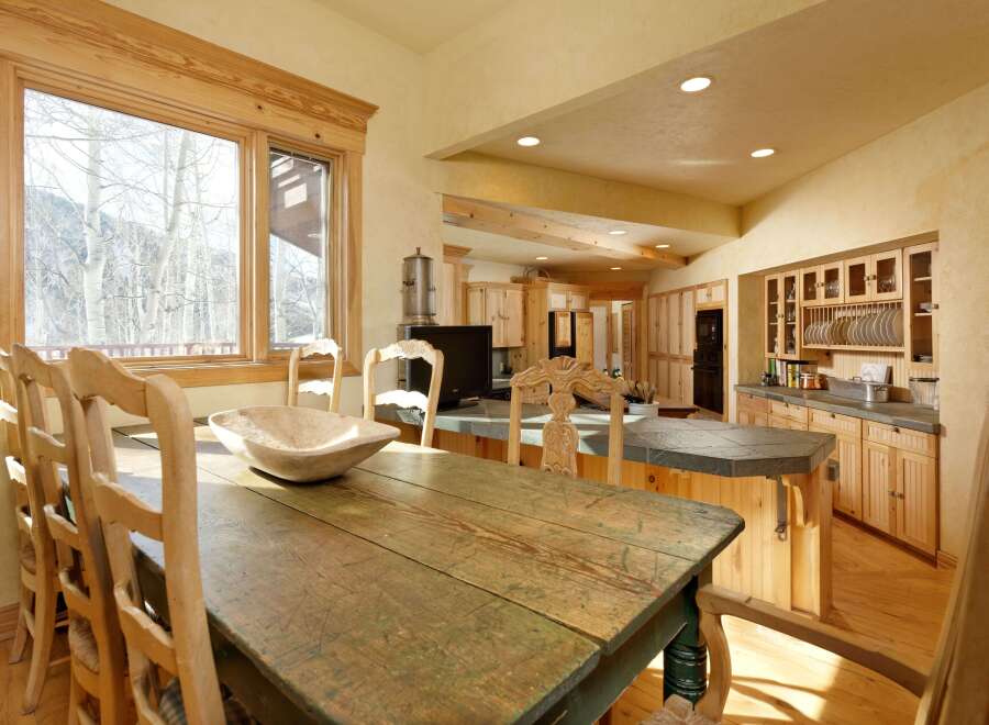 Rustic mountain home boasts a charming kitchen with knotty pine cabinets, a large farmhouse table, and a view of snow-covered trees.