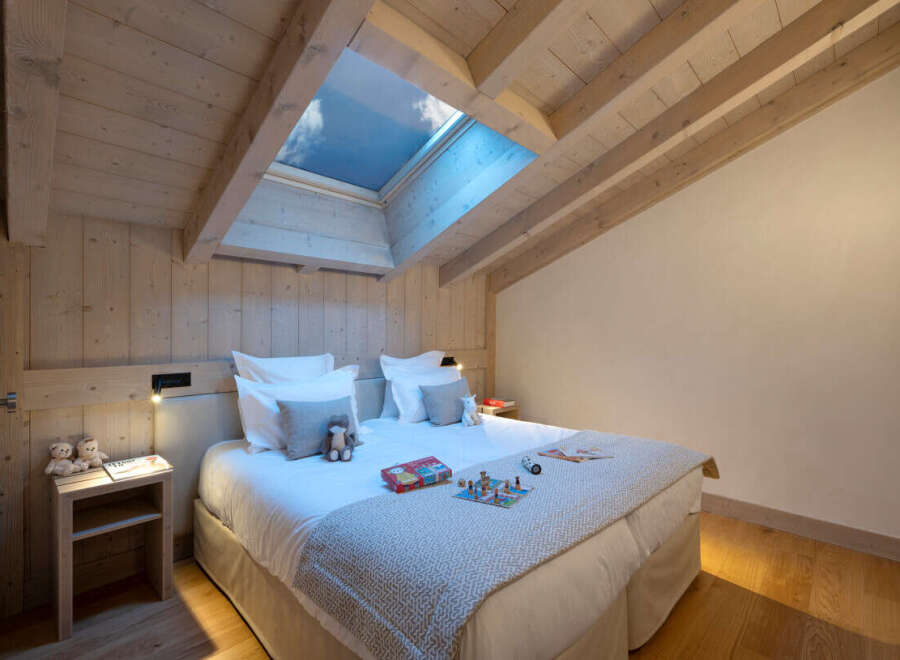Cozy attic bedroom with wood-beamed ceiling and skylights, featuring a comfortable double bed and nightstands.