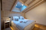 Cozy attic bedroom with wood-beamed ceiling and skylights, featuring a comfortable double bed and nightstands.