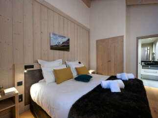 This luxurious bedroom boasts a king-size bed dressed in crisp white linens and plush dark fur throw, complemented by a stunning mountain landscape painting.