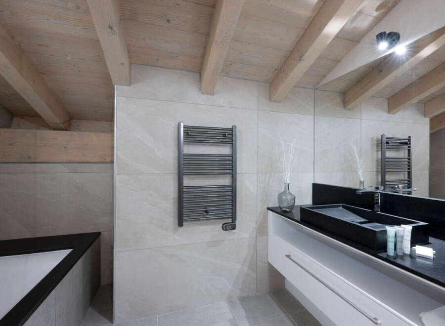 This luxurious bathroom boasts a modern design with a sleek black sink and white vanity, complemented by a heated towel rack and a spacious bathtub.