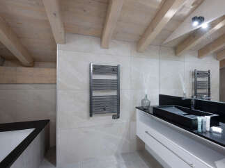 This luxurious bathroom boasts a modern design with a sleek black sink and white vanity, complemented by a heated towel rack and a spacious bathtub.