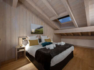 This stunning attic bedroom boasts a cozy and luxurious atmosphere, featuring a king-size bed with plush bedding and a faux fur throw.
