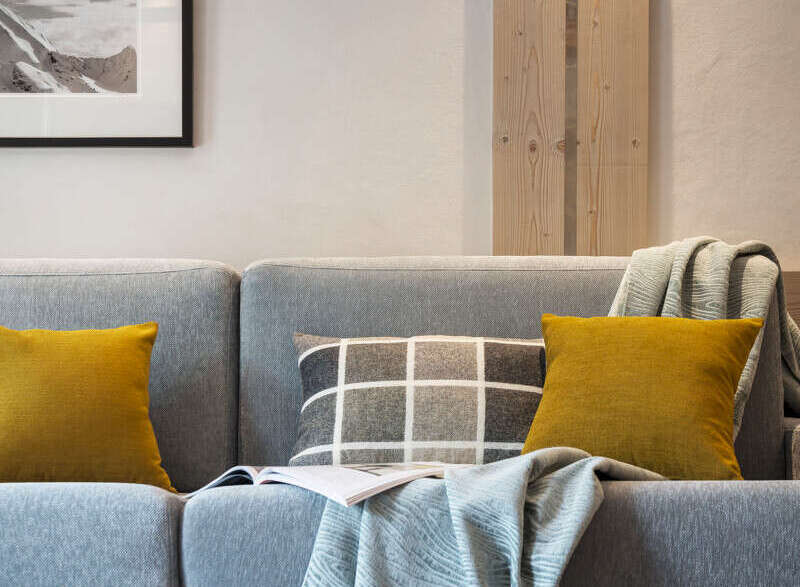 Cozy living room with a comfortable gray sofa featuring mustard yellow and gray patterned throw pillows.