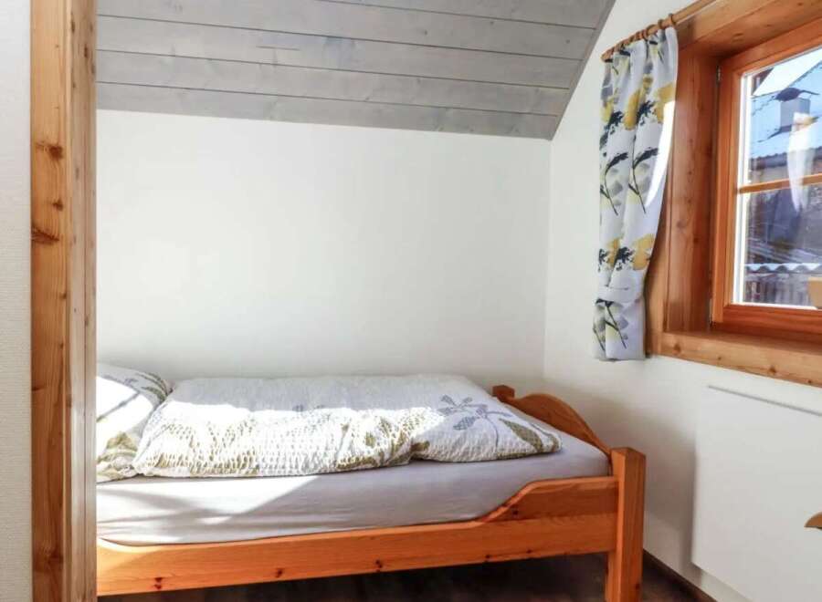 Cozy bedroom featuring a wooden bed frame and a charming window with floral curtains.